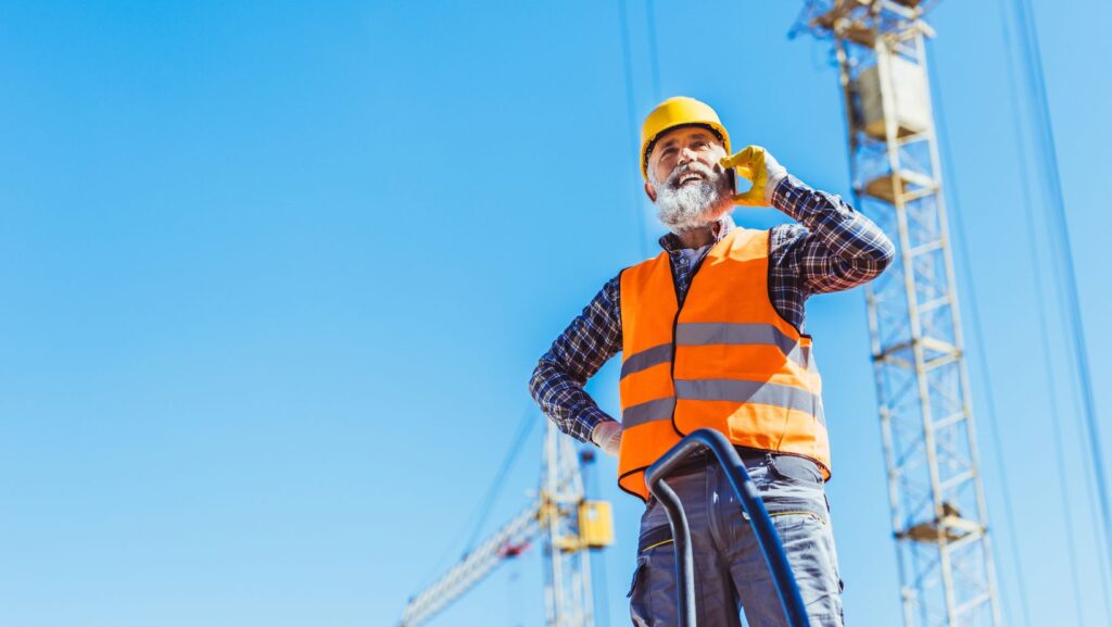 ''travailleur en construction qui parle au téléphone devant une grue. La téléphonie VoIP : un outil essentiel pour les entreprises de construction''