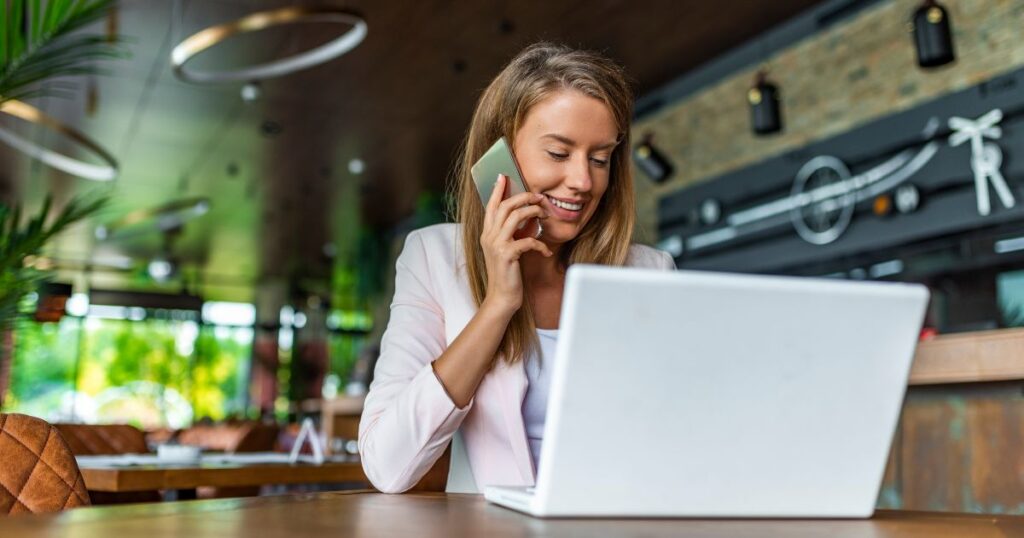 ''Une dame qui parle au téléphone et qui regarde un ordinateur en souriant''